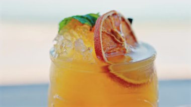 Arka planda bulanık deniz manzaralı bir masanın üzerindeki portakal kokteylini kapat.