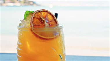 Arka planda bulanık deniz manzaralı bir masanın üzerindeki portakal kokteylini kapat.