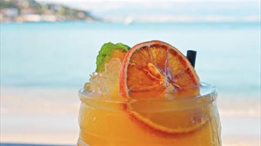 Arka planda bulanık deniz manzaralı bir masanın üzerindeki portakal kokteylini kapat.