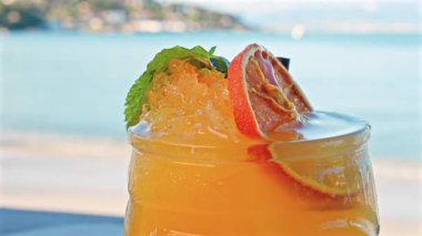 Arka planda bulanık deniz manzaralı bir masanın üzerindeki portakal kokteylini kapat.