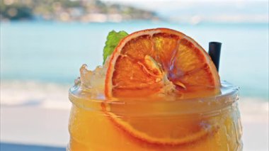 Arka planda bulanık deniz manzaralı bir masanın üzerindeki portakal kokteylini kapat.