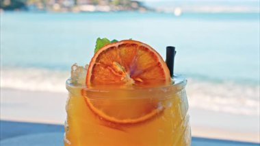 Arka planda bulanık deniz manzaralı bir masanın üzerindeki portakal kokteylini kapat.