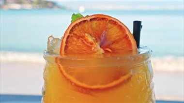 Arka planda bulanık deniz manzaralı bir masanın üzerindeki portakal kokteylini kapat.