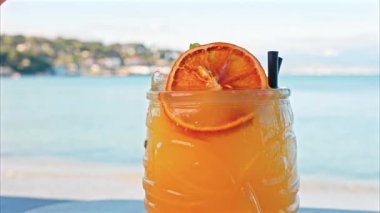Arka planda bulanık deniz manzaralı bir masanın üzerindeki portakal kokteylini kapat.