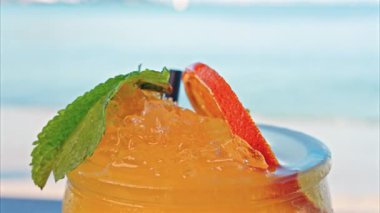 Arka planda bulanık deniz manzaralı bir masanın üzerindeki portakal kokteylini kapat.