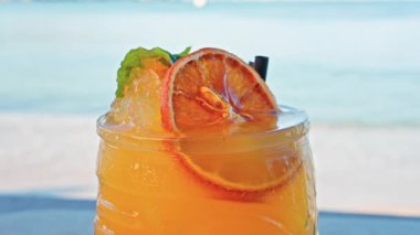 Arka planda bulanık deniz manzaralı bir masanın üzerindeki portakal kokteylini kapat.