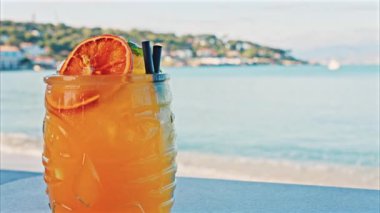 Arka planda bulanık deniz manzaralı bir masanın üzerindeki portakal kokteylini kapat.