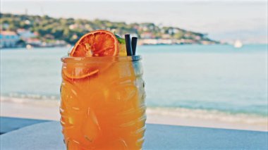 Arka planda bulanık deniz manzaralı bir masanın üzerindeki portakal kokteylini kapat.