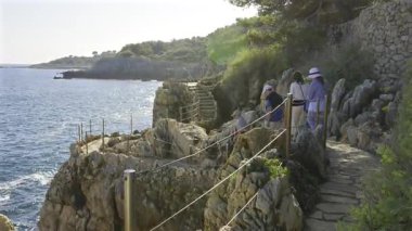 Arka planda deniz olan plaj merdivenlerinde yürüyen insanlar.