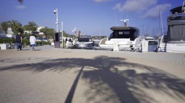 Juan-les-Pins, Fransa - 8 Nisan 2025: Güneşli bir günde limana yanaşmış beyaz teknelerin yanında yürüyen insanlar