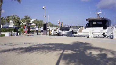 Juan-les-Pins, Fransa - 8 Nisan 2025: Güneşli bir günde limana yanaşmış beyaz teknelerin yanında yürüyen insanlar