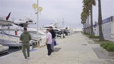 Vallauris, Fransa - 9 Nisan 2025: Bulutlu bir günde limana yanaşmış teknelerin yanında yürüyen insanlar