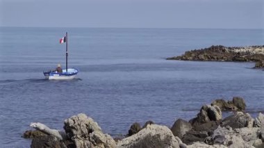 Antibes, Fransa - 25 Nisan 2025: Hareket halindeki bir teknede arka planda binalar olan bir adam