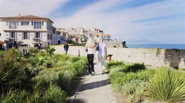 Antibes, Fransa - 27 Nisan 2025: Sahildeki farklı binaların etrafında yürüyen insanların görüntüsü