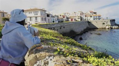 Antibes, Fransa - 27 Nisan 2025: Sahildeki farklı binaların etrafında yürüyen insanların görüntüsü