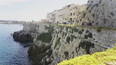 Antibes, Fransa - 27 Nisan 2025: Sahildeki farklı binaların etrafında yürüyen insanların görüntüsü