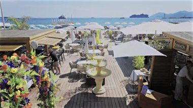 Cannes, Fransa - 28 Nisan 2025: Bir sahil restoranında güneş şemsiyesi altında çalışan insanların görüntüsü