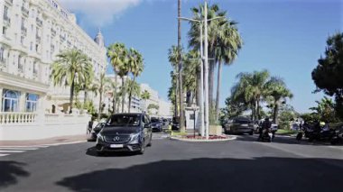 Cannes, Fransa - 28 Nisan 2025: İnsanlar ve arabalar palmiye ağaçları yakınındaki caddelerde ilerliyorlar