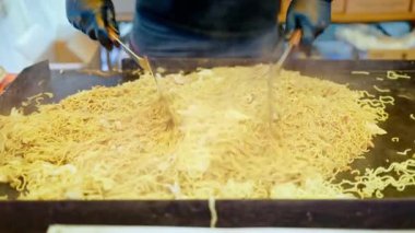 Japonya 'da bir sokak yiyecek pazarında erişteleri eritmek için metal spatula kullanan bir satıcıyı kapatın.