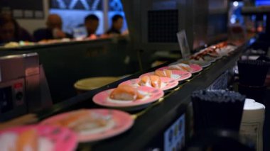 Tokyo, Japonya - 23 Nisan 2025 Restoranda hareket eden bir taşıma bandına yerleştirilmiş suşiyle tabakların kapatılması