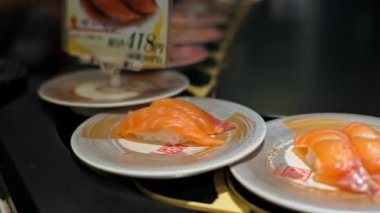 Tokyo, Japonya - 23 Nisan 2025 Restoranda hareket eden bir taşıma bandına yerleştirilmiş suşiyle tabakların kapatılması