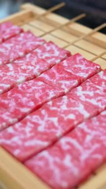 Close up of multiple pieces of Wagyu beef on a wooden tray at a street food market in Japan. Vertical