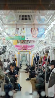 Tokyo, Japonya - 23 Nisan 2025: Metroda oturan ve ayakta duran insanlar. Dikey