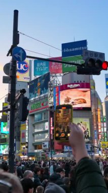 Tokyo, Japonya - 23 Nisan 2025: İnsanlar akşam Shibuya ticaret merkezinde karşıdan karşıya geçiyorlar. Dikey. Çeviri: 