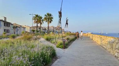 Antibes, Fransa - 29 Ağustos 2024: Arka planda Nicolas Lavarenne 'in bronz heykellerinin yanında yürüyen insanları izleyin