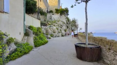 Antibes, Fransa - 29 Ağustos 2024: Sahildeki farklı binaların etrafında yürüyen insanların görüntüsü