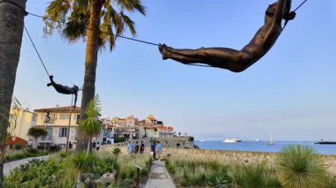Antibes, Fransa - 29 Ağustos 2024: İki palmiye ağacı arasında asılı duran mavi gökyüzü arka planında Nicolas Lavarenne 'in bronz heykeli