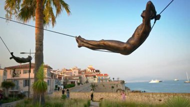 Antibes, Fransa - 29 Ağustos 2024: İki palmiye ağacı arasında asılı duran mavi gökyüzü arka planında Nicolas Lavarenne 'in bronz heykeli