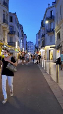 Cannes, Fransa - 24 Ağustos 2024: İnsanlar akşamları şehrin sokaklarında mağazaların yakınında yürüyorlar. Dikey