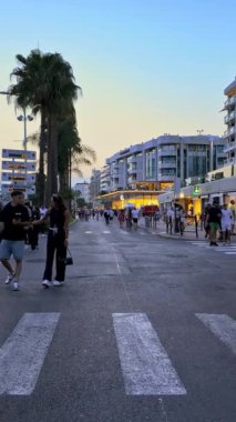 Cannes, Fransa - 24 Ağustos 2024: İnsanlar akşamları şehrin sokaklarında mağazaların yakınında yürüyorlar. Dikey
