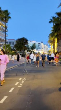 Cannes, Fransa - 24 Ağustos 2024: Akşamları Croisette Bulvarı 'nda yürüyen insanlar. Dikey