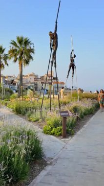 Antibes, Fransa - 29 Ağustos 2024: Arka planda Nicolas Lavarenne 'in bronz heykellerinin yanında yürüyen insanları izleyin. Dikey