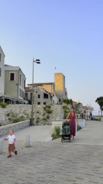 Antibes, Fransa - 29 Ağustos 2024: Kıyıdaki farklı binaların yakınında yürüyen insanları görmek. Dikey