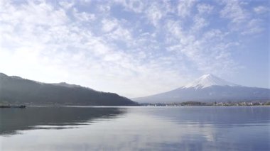 Sakin sular, bulutlarla dolu çarpıcı bir gökyüzüne karşı Fuji Dağı 'nın mükemmel bir yansımasını sağlar. Bu sakin yer doğanın güzelliğini gösteriyor ve huzurlu bir atmosfer sunuyor. Kawaguchiko Gölü
