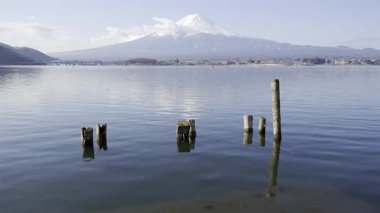 Fuji Dağı, sakin suların zirvesini yansıttığı gibi ihtişamlı bir şekilde arka planda duruyor. Tahta direkler gölden çıkar ve Japonya 'daki bu resmedilmeye değer manzaraya odaklanırlar. Kawaguchiko Gölü