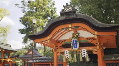 Tarihi bir tapınağın kırmızı binaları. Sitede canlı renkler ve Japon kültürünü temsil eden karmaşık tasarımlar yer alıyor. Metin çevirisi: 