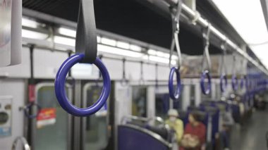 Bir toplu taşıma treninin içinde, tavandan sarkan mavi kollar, yolculara destek sağlıyordu. Kyoto, Japonya