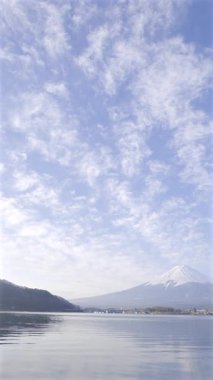 A breathtaking view of Mount Fuji surrounded by clear skies and floating clouds over Lake Kawaguchi shows nature's tranquil beauty as day breaks. Japan. Vertical video