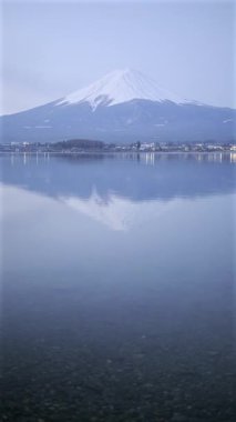 Durgun bir göl üzerinde karla kaplı Fuji dağı durgun suda çarpıcı bir yansıma yaratıyor. Sahne alacakaranlık saatlerinde doğanın güzelliğini yakalar. Dikey video