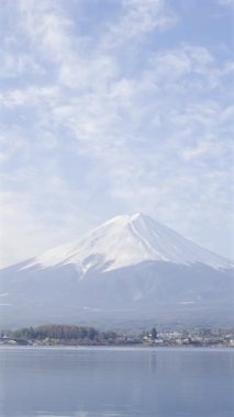 Fuji Dağı manzaranın üzerinde görkemli bir şekilde yükselir, karla kaplı zirvesi parlak mavi bir gökyüzünün altında parıldar. Kawaguchi Gölü, Japonya. Dikey video