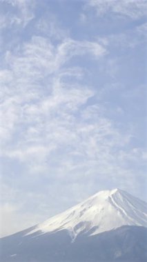 Fuji Dağı 'nın açık gökyüzü ve Kawaguchi Gölü üzerinde yüzen bulutlarla çevrili nefes kesen manzarası, doğanın gün ağarırken dingin güzelliğini gösteriyor. Japonya. Dikey video