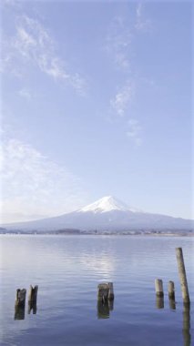 Fuji Dağı 'nın açık gökyüzü ve Kawaguchi Gölü üzerinde yüzen bulutlarla çevrili nefes kesen manzarası, doğanın gün ağarırken dingin güzelliğini gösteriyor. Japonya. Dikey video