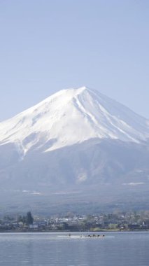 Fuji Dağı 'nın açık gökyüzü ve Kawaguchi Gölü üzerinde yüzen bulutlarla çevrili nefes kesen manzarası, doğanın gün ağarırken dingin güzelliğini gösteriyor. Japonya. Dikey video