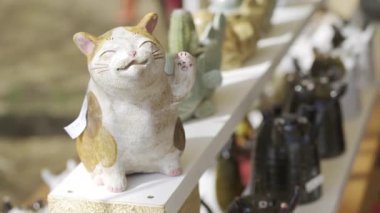Fujikawaguchiko, Japonya - 9 Nisan 2025: Neşeli bir ifadeye sahip büyüleyici bir seramik kedi heykelciği bir zanaatkar pazarında çeşitli el yapımı eşyalar arasında yer almaktadır..