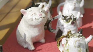 Fujikawaguchiko, Japonya - 9 Nisan 2025: Keyifli bir seramik kedi heykelciği, rahat bir dükkânda kaprisli hayvan çaydanlıklarıyla çevriliyken parlak bir şekilde gülümsüyor.
