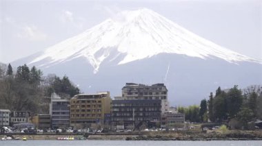 Fujikawaguchiko, Japonya - 9 Nisan 2025: Fuji Dağı Japonya 'da göl kenarındaki otellerin üstündeki karlı zirvelerle görkemli bir şekilde ayakta duruyor. Berrak bahar gökyüzü bu dingin manzaraya çarpıcı bir zemin sağlar..